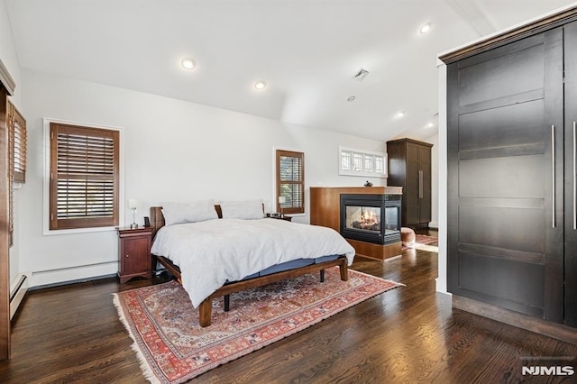 bedroom with dark wood-style floors, multiple windows, vaulted ceiling, and a multi sided fireplace