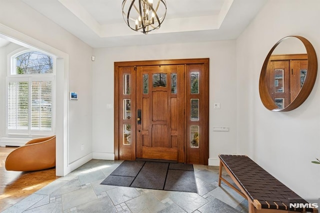 entrance foyer with baseboards, a tray ceiling, a chandelier, and stone tile floors