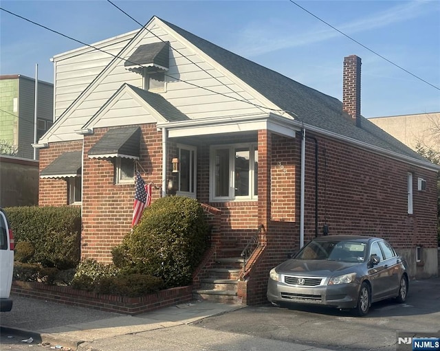 view of front of home with brick siding, roof with shingles, and a chimney