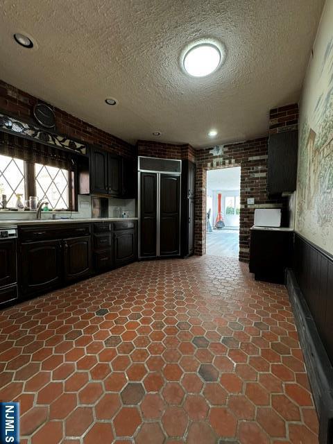 kitchen with paneled fridge, a wainscoted wall, brick wall, light countertops, and a textured ceiling