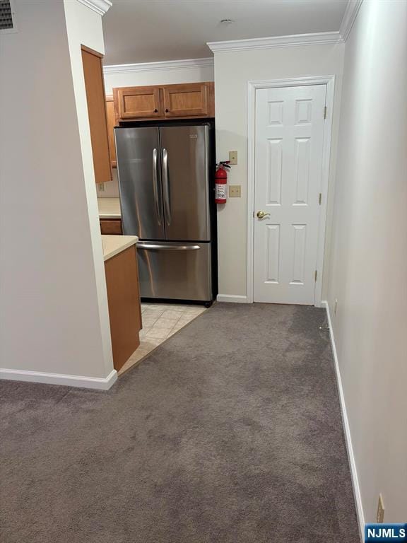 kitchen featuring light carpet, baseboards, freestanding refrigerator, brown cabinets, and crown molding