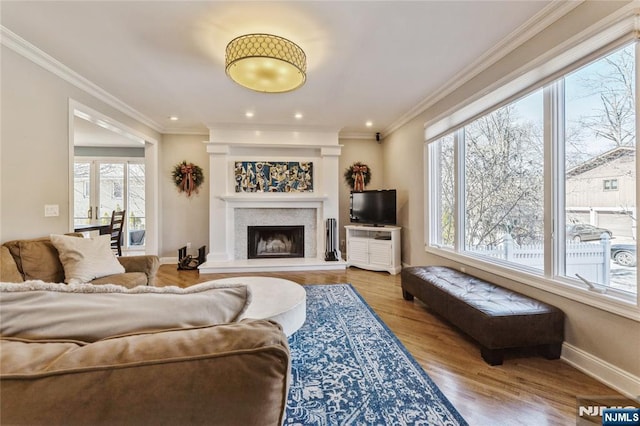 living area with a fireplace with raised hearth, crown molding, baseboards, and wood finished floors