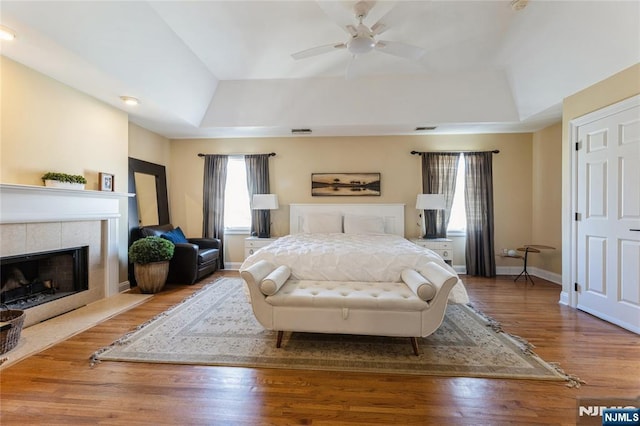 bedroom featuring a tiled fireplace, baseboards, a raised ceiling, and wood finished floors