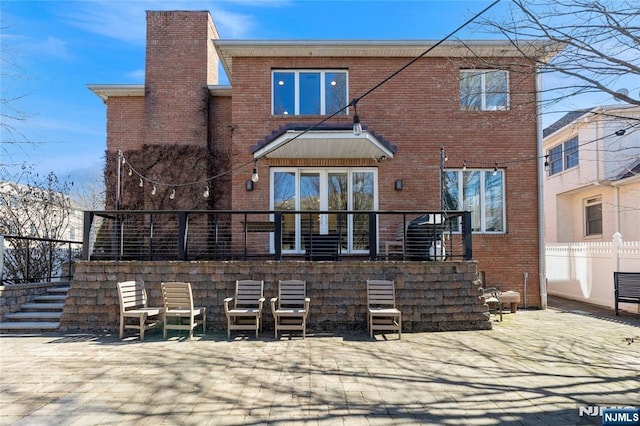 back of house with a patio area, stairs, a chimney, and brick siding