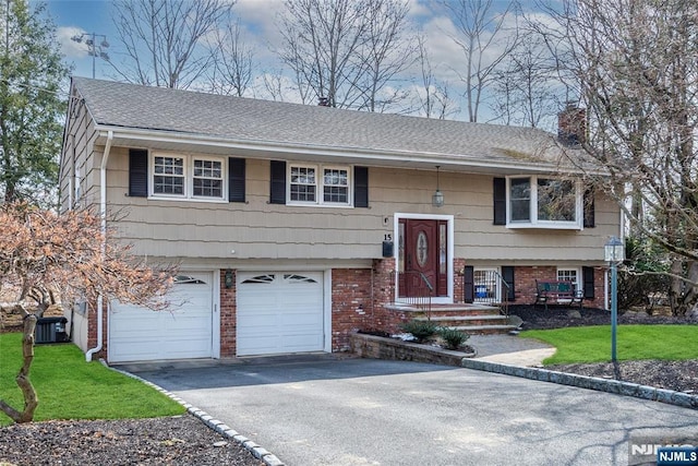 split foyer home featuring central AC unit, a chimney, aphalt driveway, an attached garage, and brick siding