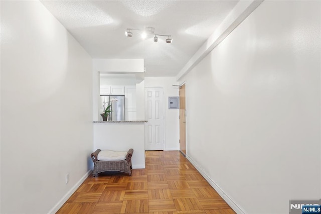 corridor featuring a textured ceiling, electric panel, and baseboards