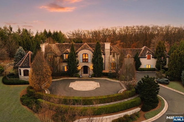 french country style house with stone siding, curved driveway, and a chimney