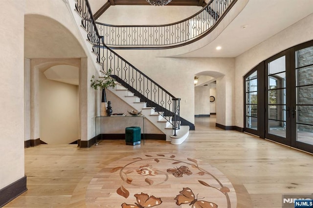 entrance foyer featuring baseboards, arched walkways, wood finished floors, a high ceiling, and french doors