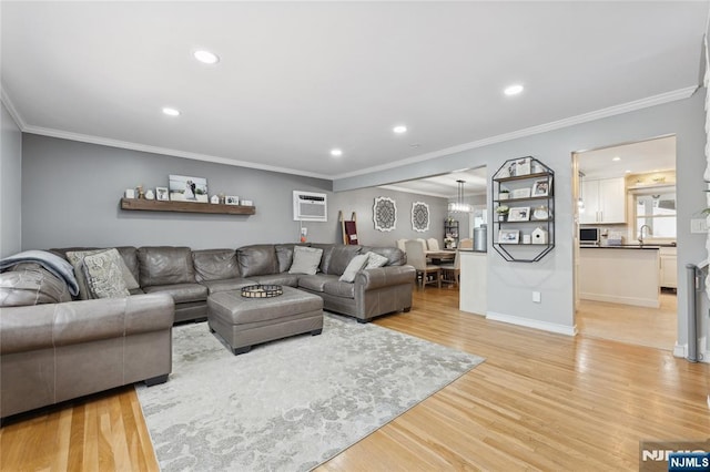 living room featuring a wall unit AC, light wood-style flooring, recessed lighting, baseboards, and crown molding