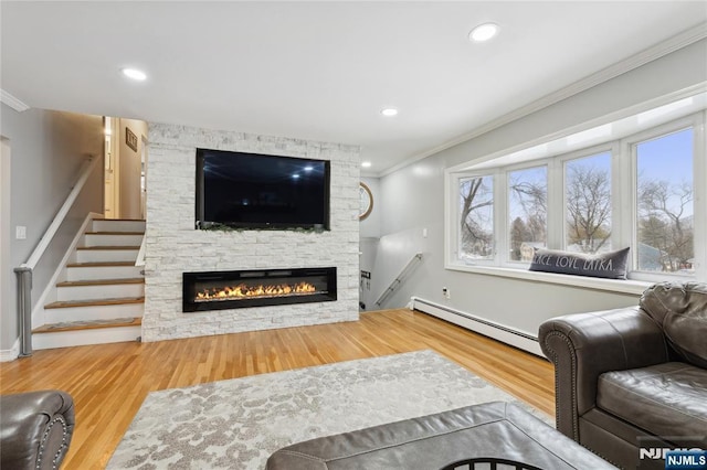 living area with a fireplace, a baseboard heating unit, wood finished floors, and ornamental molding