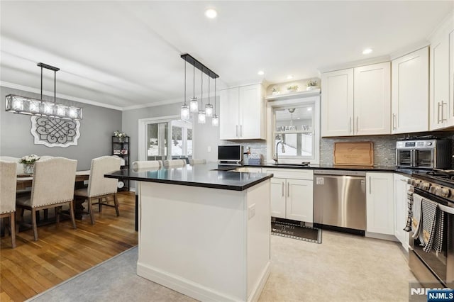 kitchen featuring stainless steel appliances, dark countertops, white cabinets, and decorative light fixtures