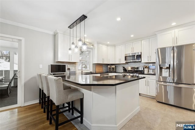 kitchen featuring stainless steel appliances, dark countertops, pendant lighting, and white cabinetry