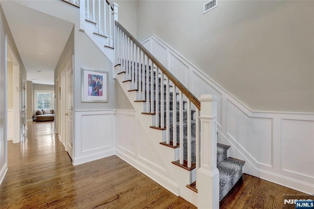 staircase with visible vents, a decorative wall, and wood finished floors