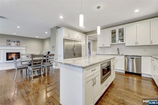 kitchen with visible vents, a glass covered fireplace, dark wood-style flooring, built in appliances, and a sink