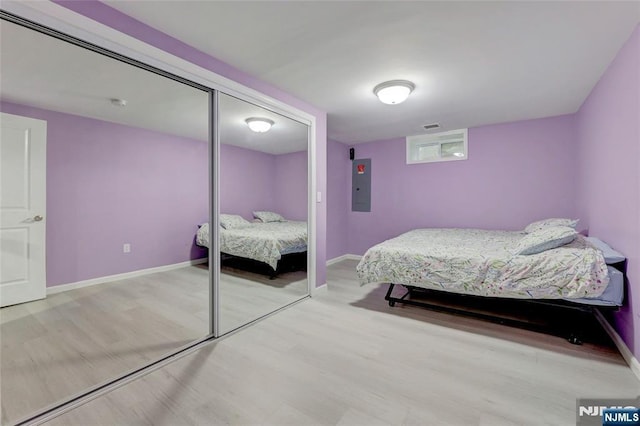 bedroom featuring electric panel, visible vents, baseboards, light wood-style floors, and a closet