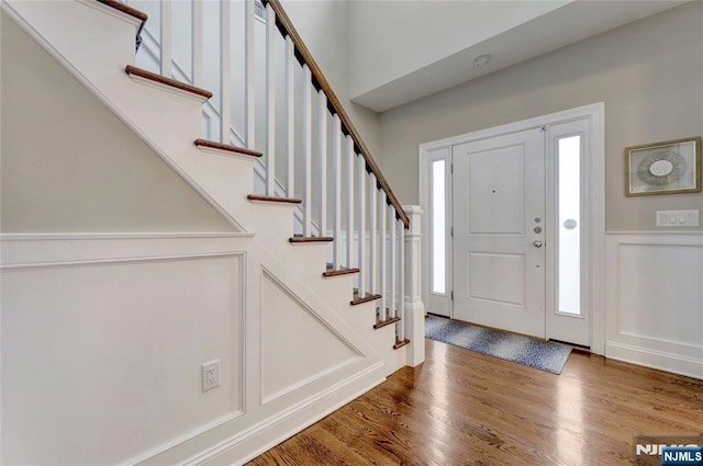 entryway featuring a wainscoted wall, a decorative wall, stairway, and wood finished floors