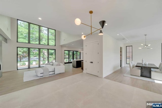 living area with a chandelier, light tile patterned flooring, recessed lighting, a towering ceiling, and baseboards