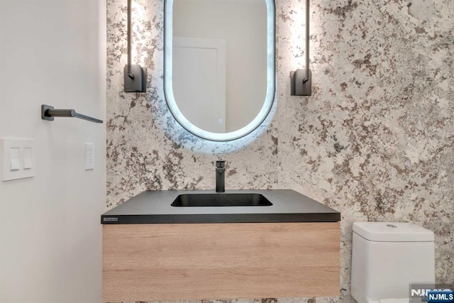 bathroom featuring toilet, vanity, and wallpapered walls