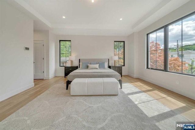 bedroom featuring light wood finished floors, a tray ceiling, baseboards, and recessed lighting