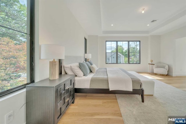 bedroom featuring baseboards, visible vents, a tray ceiling, light wood-style floors, and recessed lighting