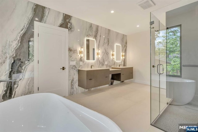 full bath with stone wall, a freestanding tub, visible vents, vanity, and tile walls