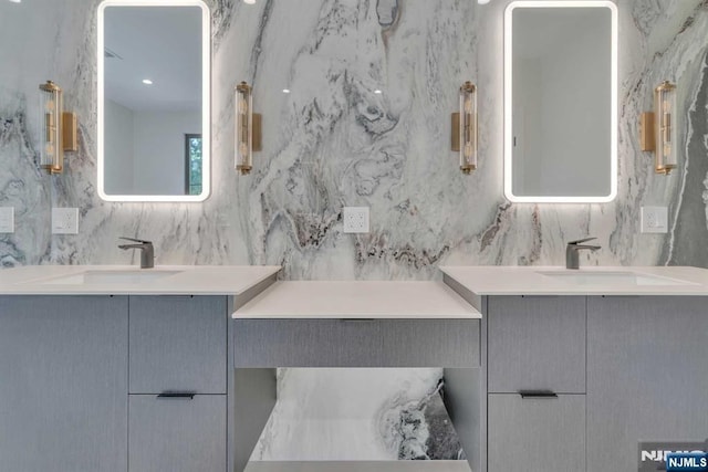 full bath featuring tile walls, two vanities, and a sink