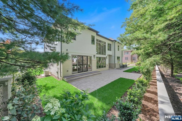 rear view of house featuring central AC, a yard, a patio area, and stucco siding