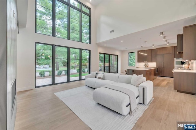 living room featuring light wood-style flooring, recessed lighting, a high ceiling, visible vents, and baseboards