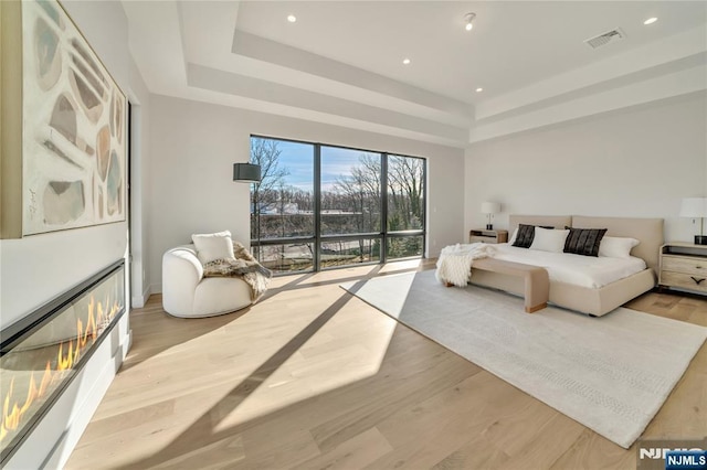 bedroom featuring access to exterior, a tray ceiling, visible vents, and light wood-style flooring