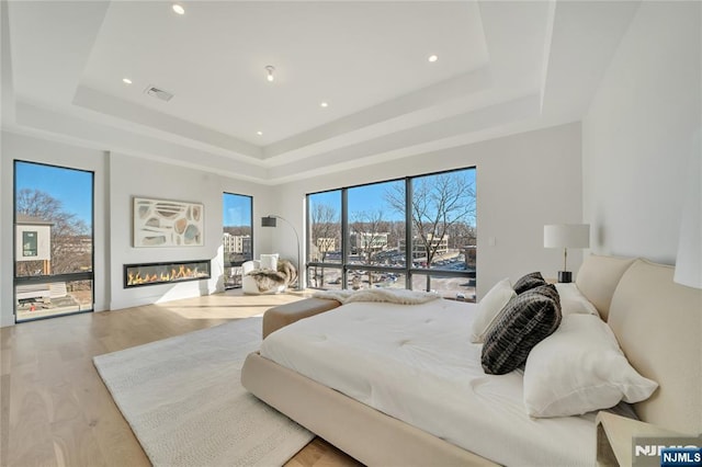 bedroom with access to outside, a raised ceiling, visible vents, and light wood-style floors