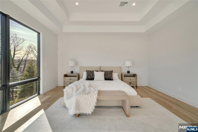 bedroom with light wood-type flooring, a raised ceiling, and visible vents