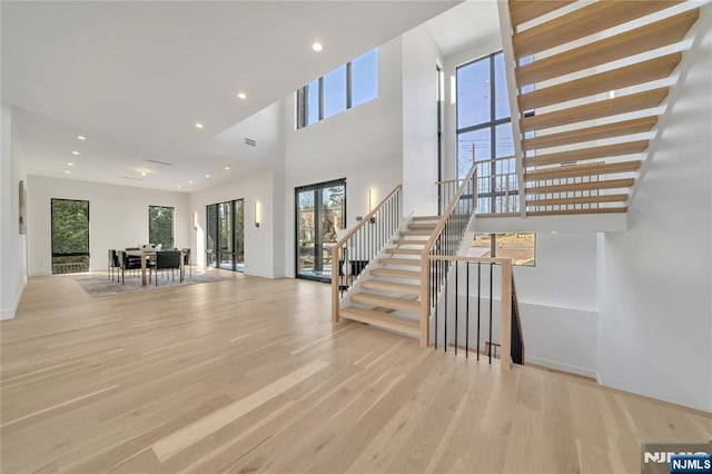 foyer entrance with stairs, a towering ceiling, light wood-style flooring, and recessed lighting