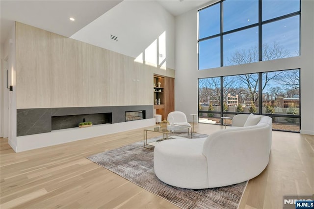 living area with a fireplace with raised hearth, recessed lighting, visible vents, built in features, and light wood-type flooring