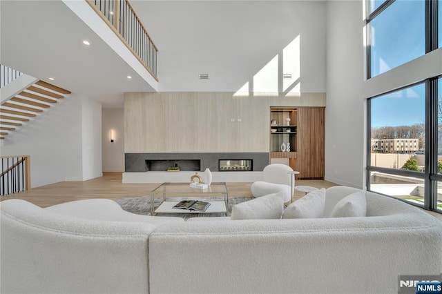 living area with recessed lighting, visible vents, a towering ceiling, a glass covered fireplace, and light wood-type flooring