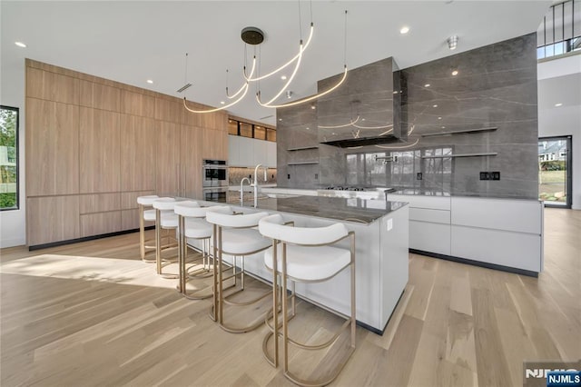 kitchen featuring white cabinets, a large island with sink, wall chimney range hood, and modern cabinets