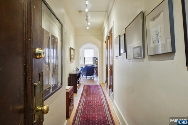 hallway featuring arched walkways, rail lighting, and baseboards