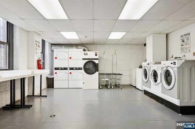 common laundry area with washer and clothes dryer, concrete block wall, and stacked washer / drying machine