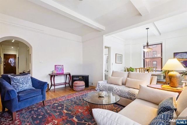 living area featuring arched walkways, beam ceiling, and wood finished floors