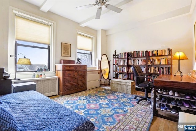 bedroom featuring beam ceiling, radiator heating unit, and wood finished floors