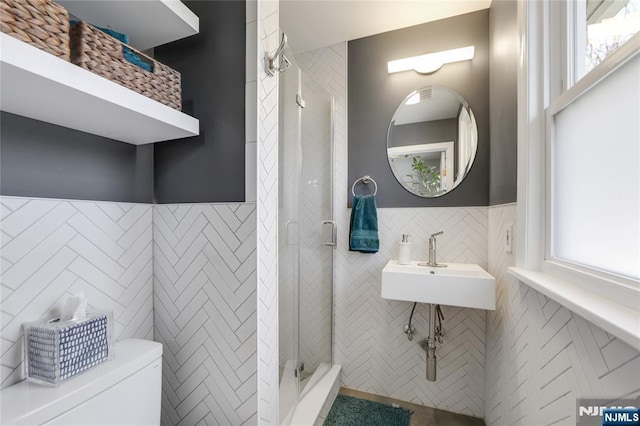 bathroom with toilet, a sink, tile walls, wainscoting, and a stall shower