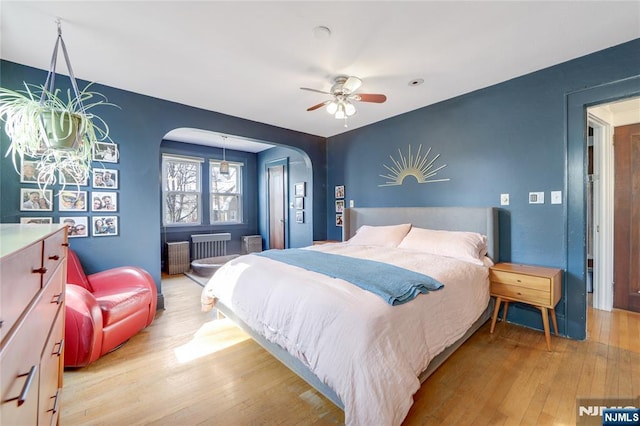 bedroom featuring arched walkways, ceiling fan, and light wood-style flooring