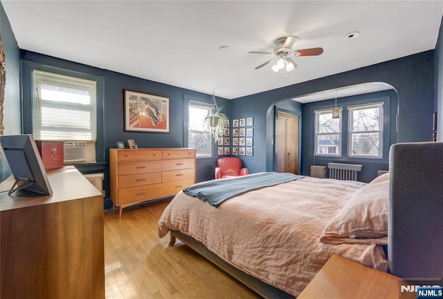 bedroom featuring light wood-style floors, arched walkways, and multiple windows