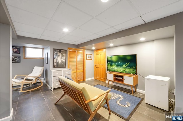 living area with baseboards, a paneled ceiling, and tile patterned floors