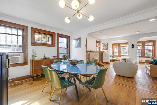 dining space featuring arched walkways, crown molding, light wood finished floors, and an inviting chandelier