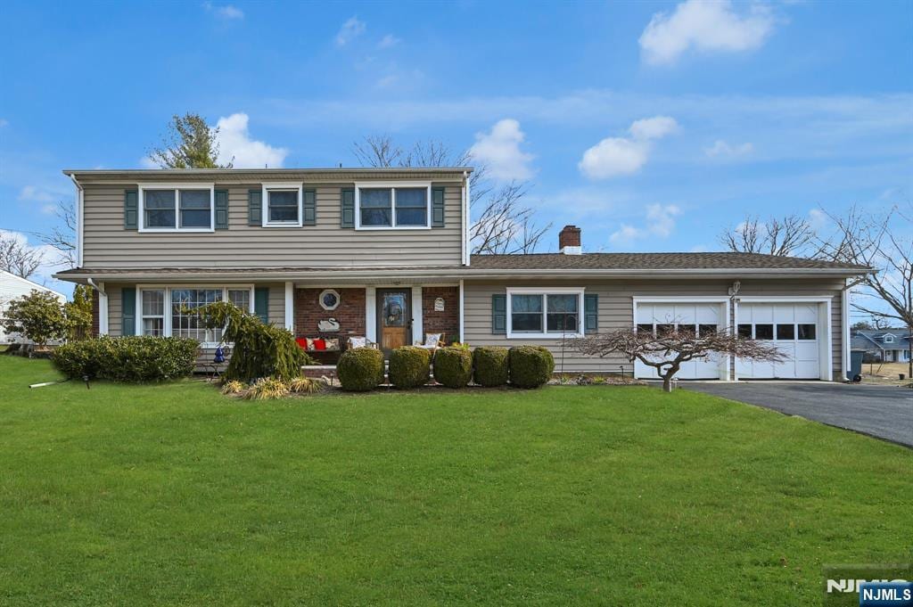 view of front of home featuring a garage, a front yard, driveway, and a chimney