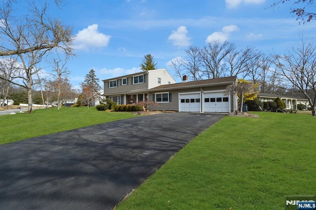 colonial house featuring an attached garage, a chimney, aphalt driveway, and a front yard