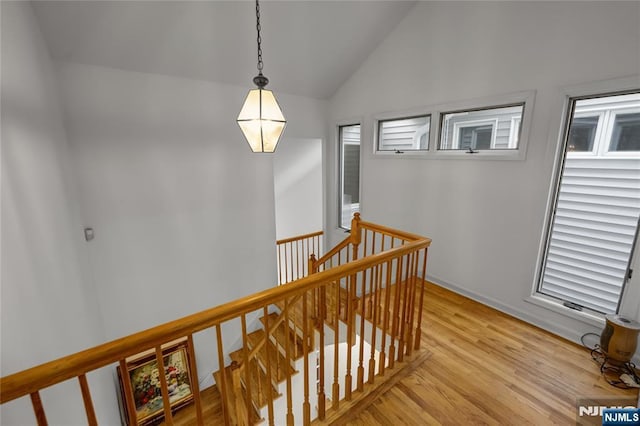 hall with vaulted ceiling, light wood-type flooring, and an upstairs landing