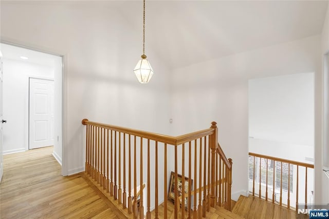 hallway featuring light wood-style flooring, baseboards, vaulted ceiling, and an upstairs landing