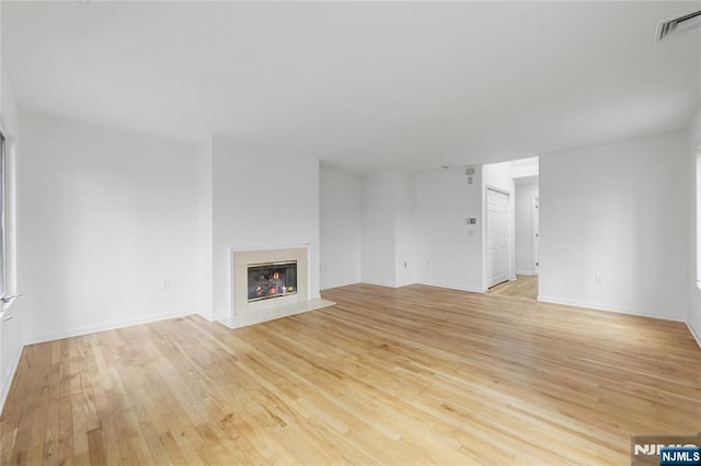 unfurnished living room with baseboards, visible vents, a fireplace, and light wood finished floors