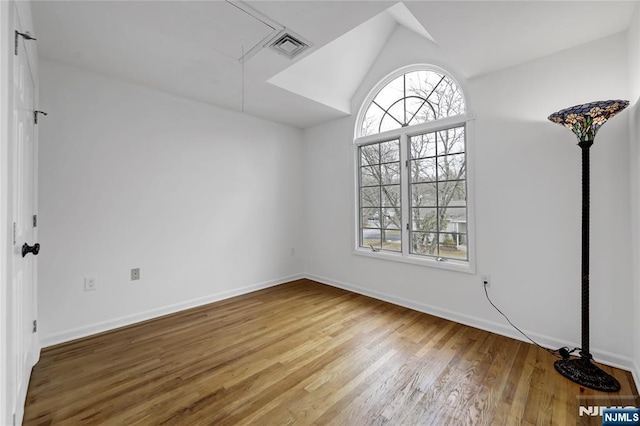 spare room featuring vaulted ceiling, wood finished floors, attic access, and a healthy amount of sunlight